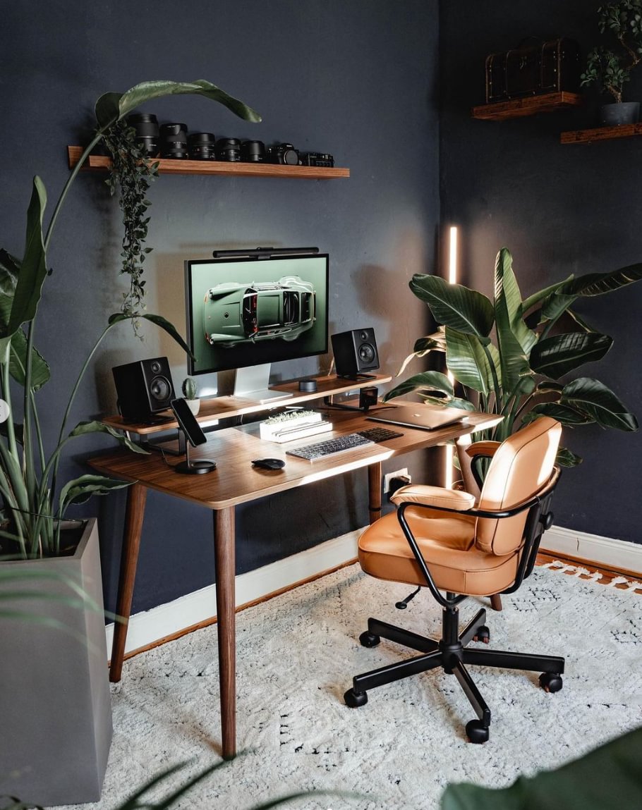 A home office with a wooden desk, a brown leather desk chair and camera lenses on a shelf