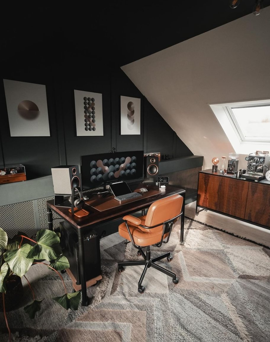 A modern desk with wall prints, dark walls and a brown leather chair