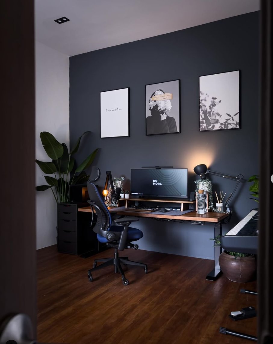 A home office with a desk, black feature wall and wall prints