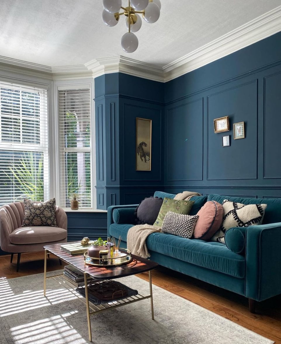 A blue velvet sofa in a living room with the same color blue panelled wall.