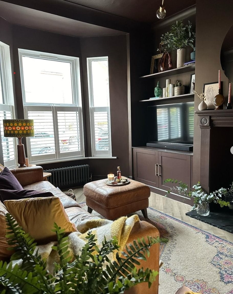 A living room with dark burgundy walls, light rug, light brown sofa and bay windows