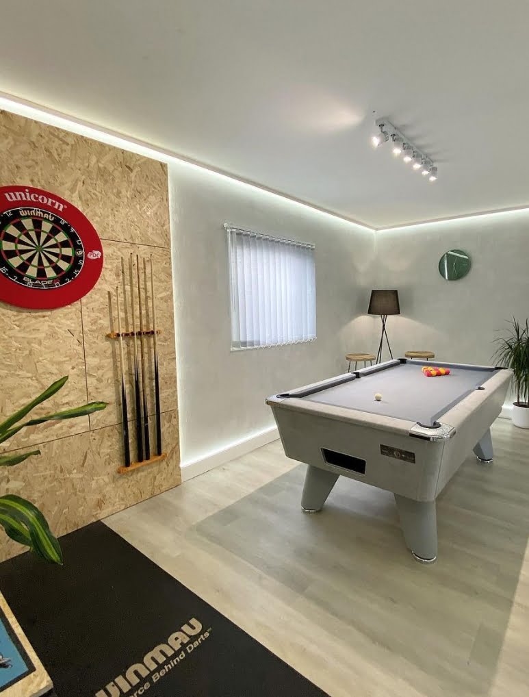 A games room with a dart board, pool table and a wooden floor