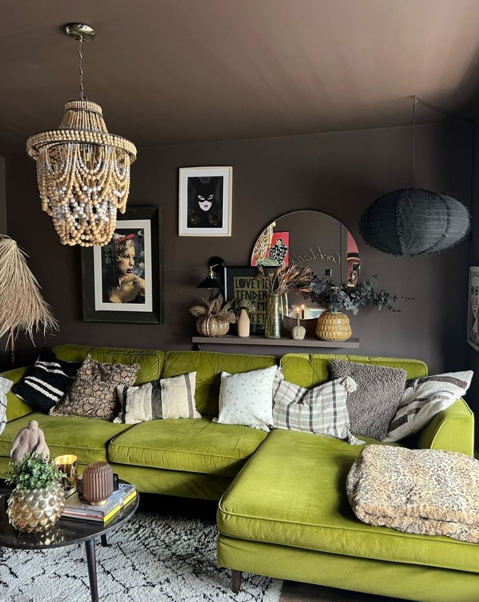 A green sofa with neutral pillows, in a dark living room