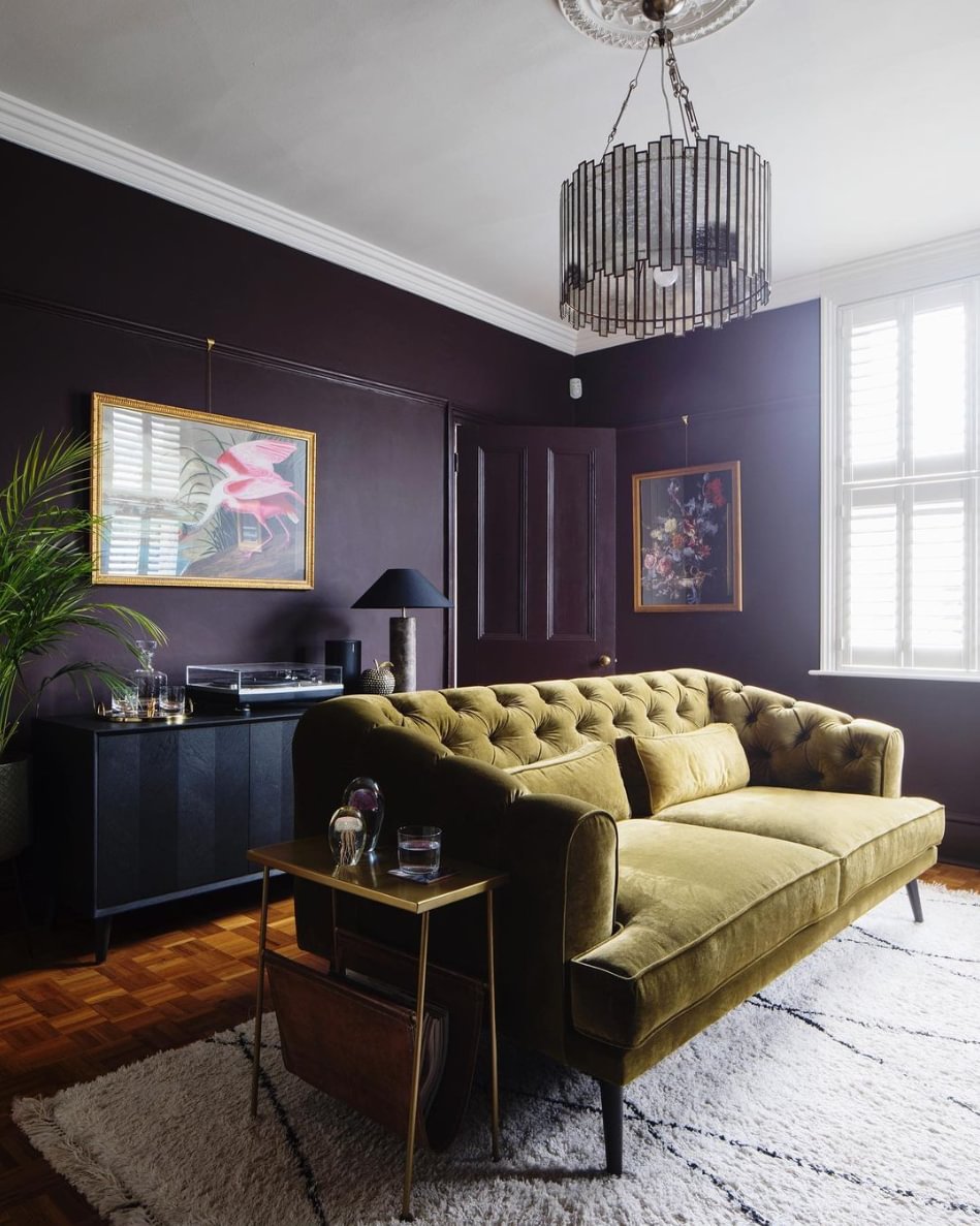 A dark purple walled living room, with a wooden floor, rug and green sofa