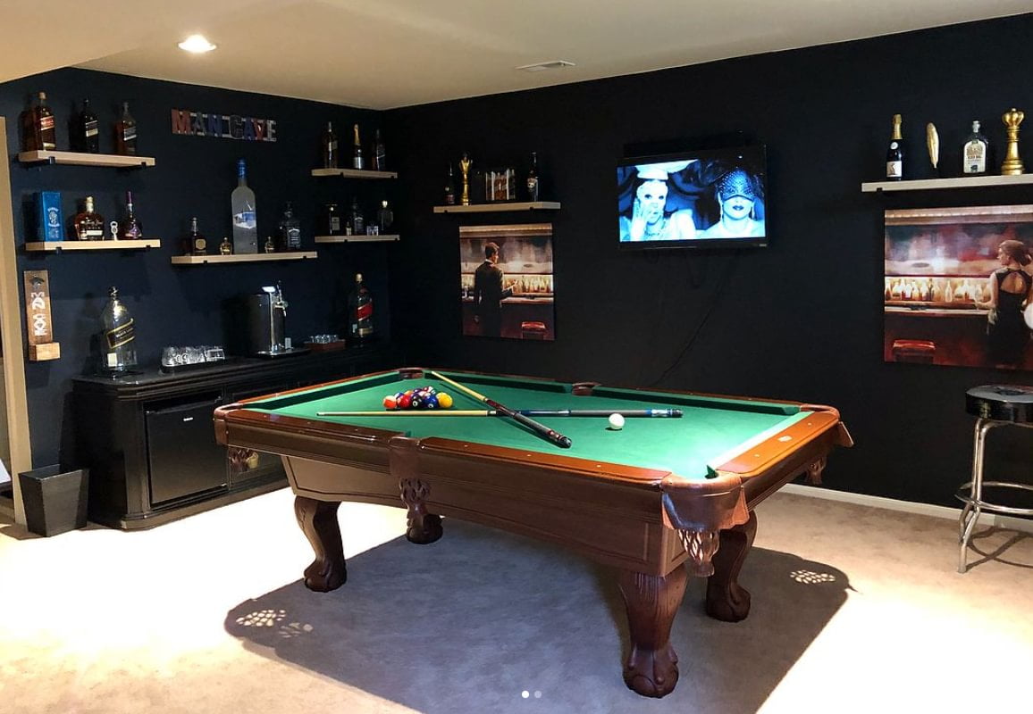 A pool table in a room with dark walls and light carpet